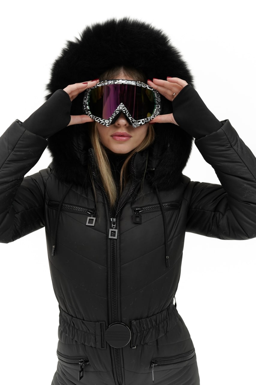 Person wearing a black winter coat with a fur-lined hood, holding ski goggles.
