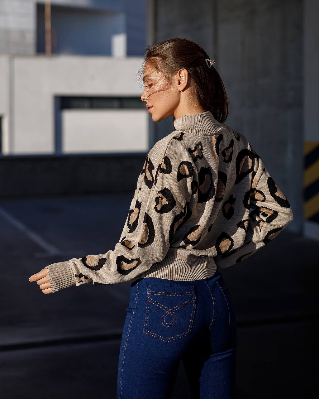Woman wearing a leopard print sweater and blue jeans standing outdoors.
