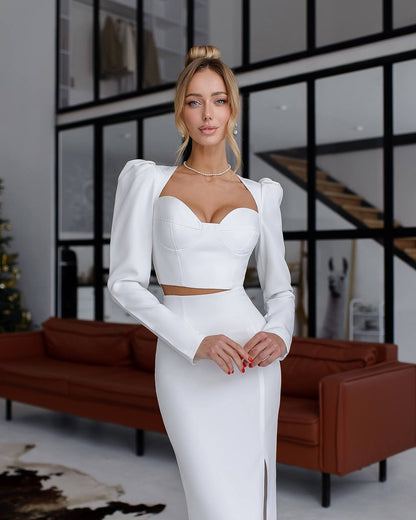 Woman in a white outfit standing in a modern indoor setting with a brown sofa and glass walls.