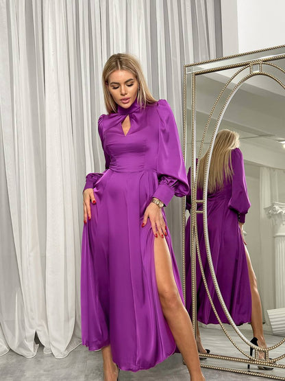 Woman in a purple dress standing in front of a mirror with white curtains in the background
