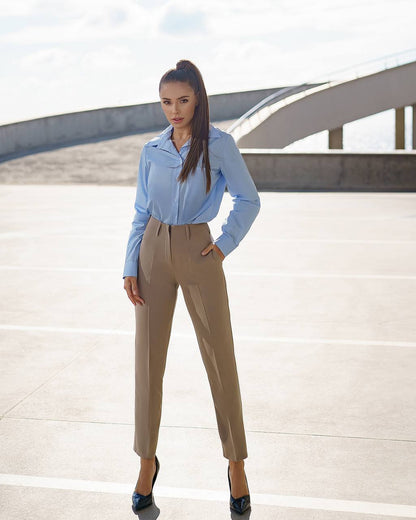Woman wearing a light blue shirt and beige pants standing on a rooftop.