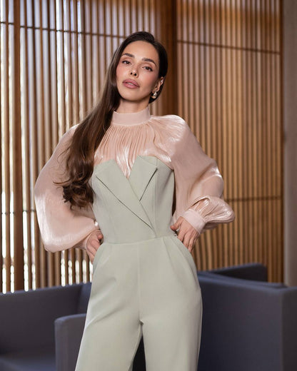 Woman wearing a light green jumpsuit with a beige blouse against a wooden panel background