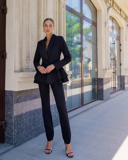 Woman in a black suit standing in front of a building with large windows.