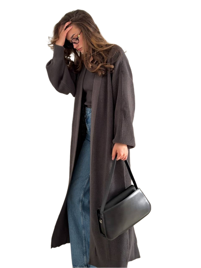 Woman wearing a long dark coat holding a black handbag on a white background