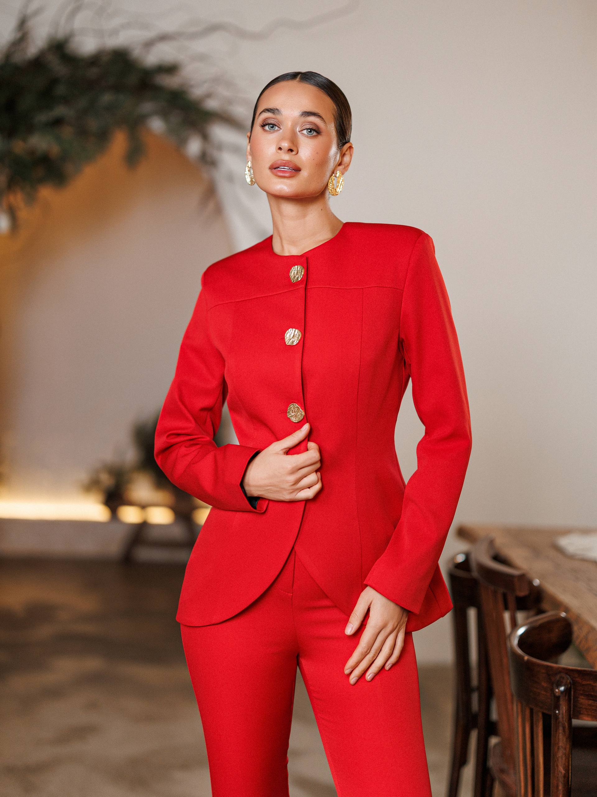 Woman wearing a red suit standing in an indoor setting with blurred background