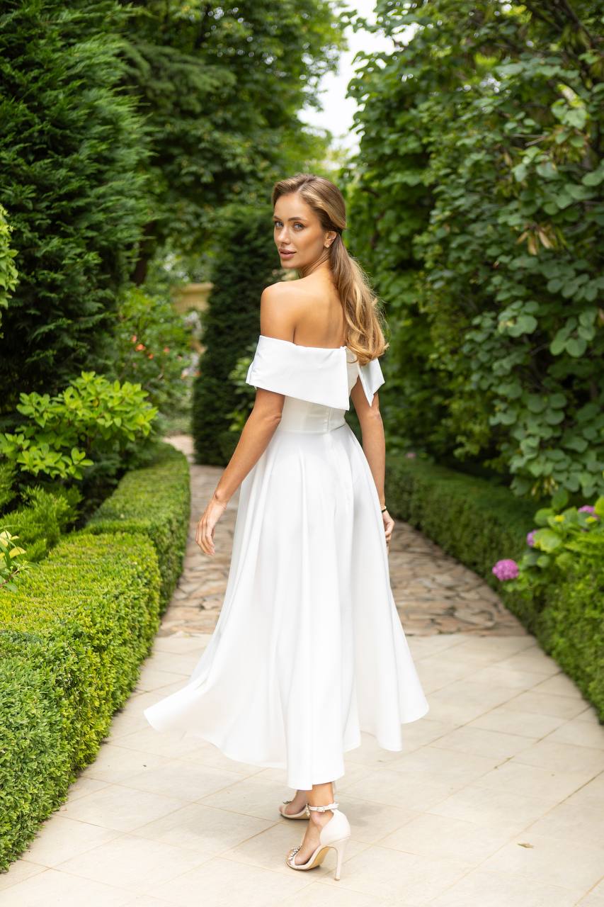 Woman in a white off-shoulder dress walking through a garden path.