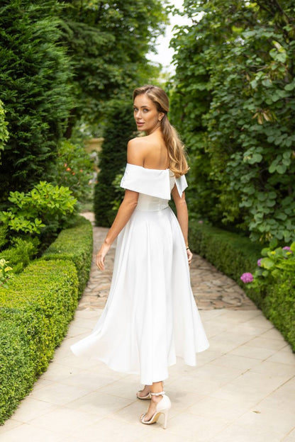 Woman in a white off-shoulder dress walking through a garden path.