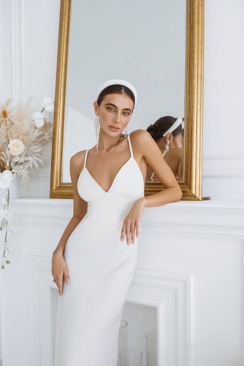 Woman in a white dress standing in front of a mirror with floral decorations.