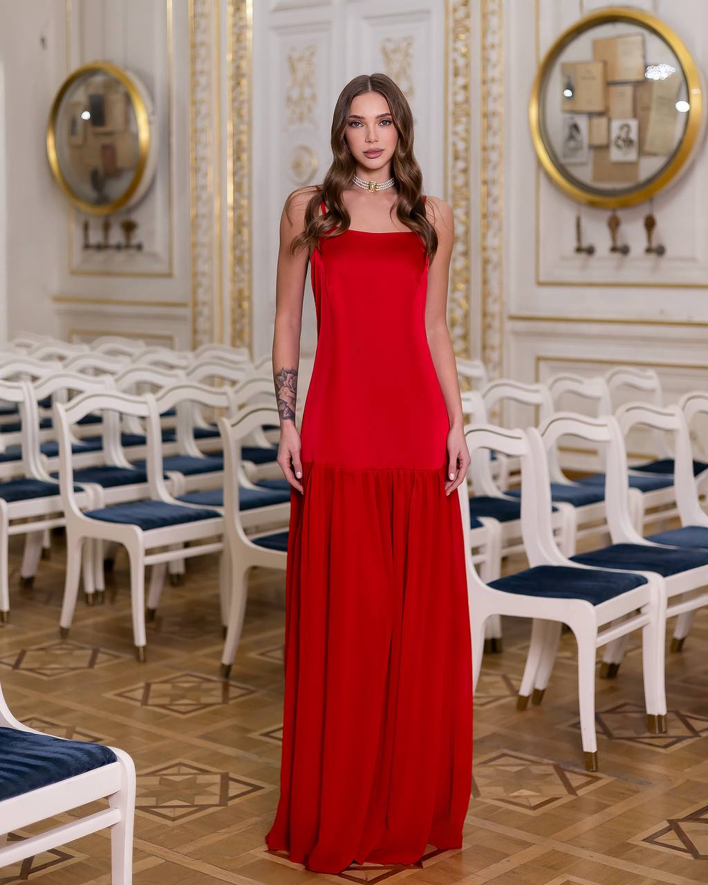 Woman in a red dress standing in an elegant room with white chairs and gold decorations.