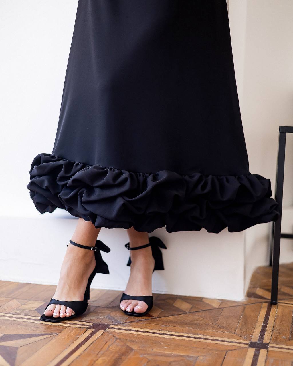 Black ruffled skirt worn by a person on a wooden floor.