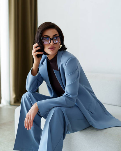 Woman in a blue suit sitting on a white couch with a neutral background
