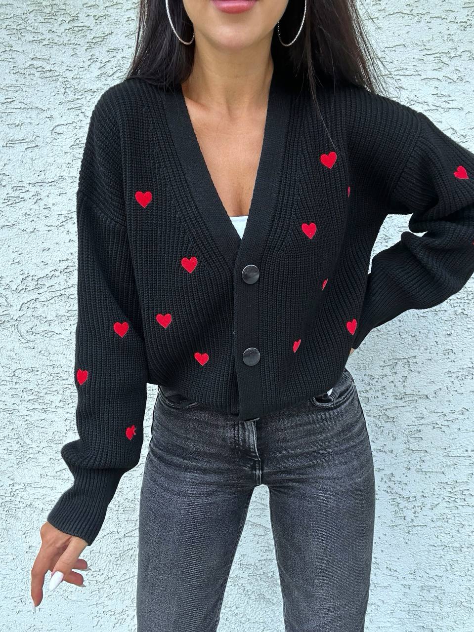 Person wearing a black cardigan with red heart patterns against a light gray background