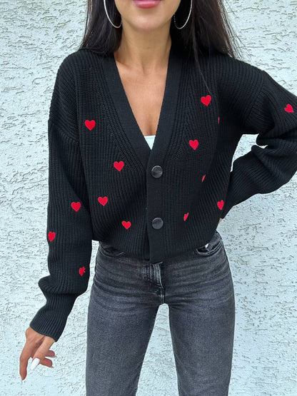Person wearing a black cardigan with red heart patterns against a light gray background