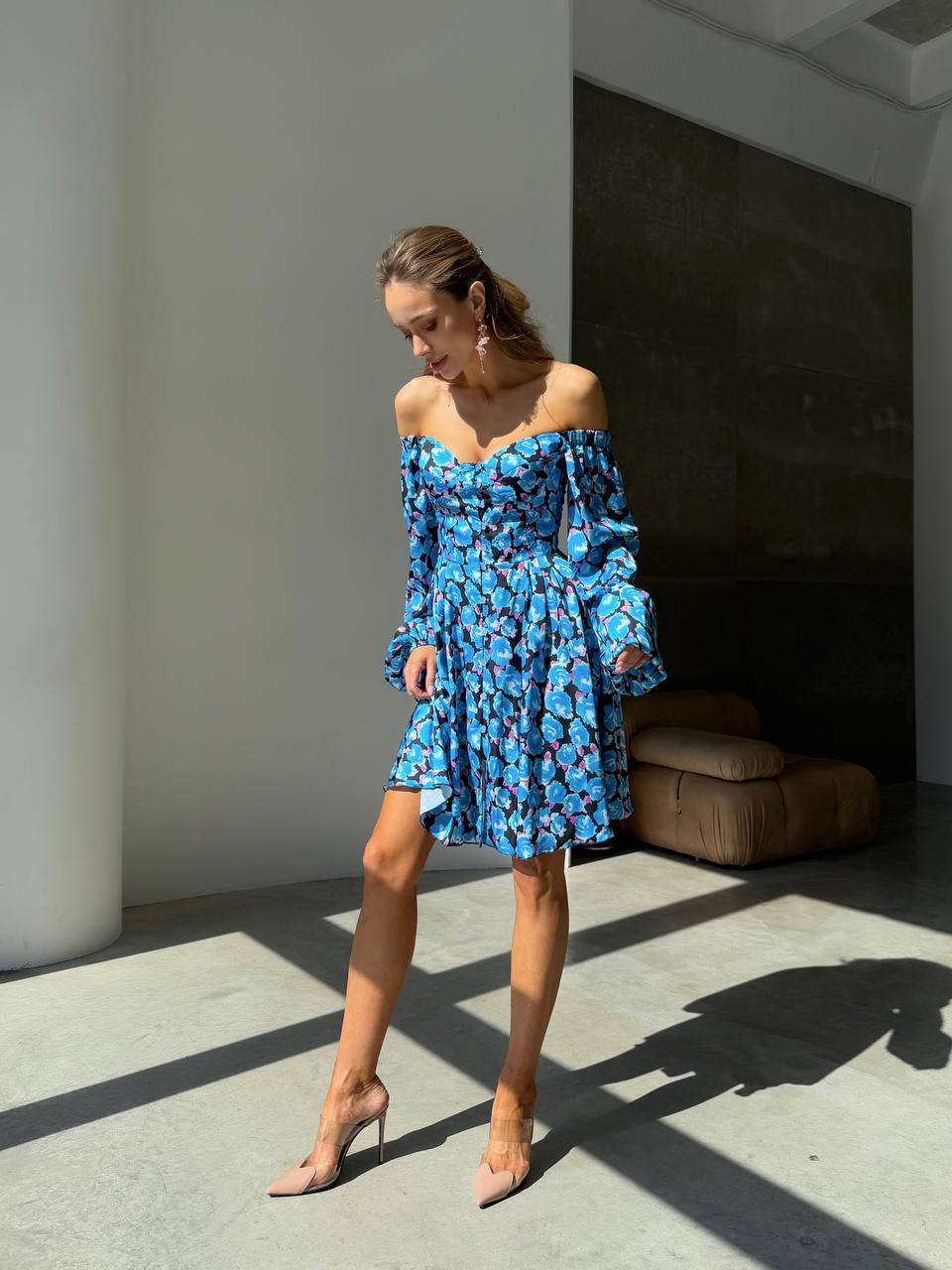 Woman wearing a blue floral dress standing in a sunlit room.