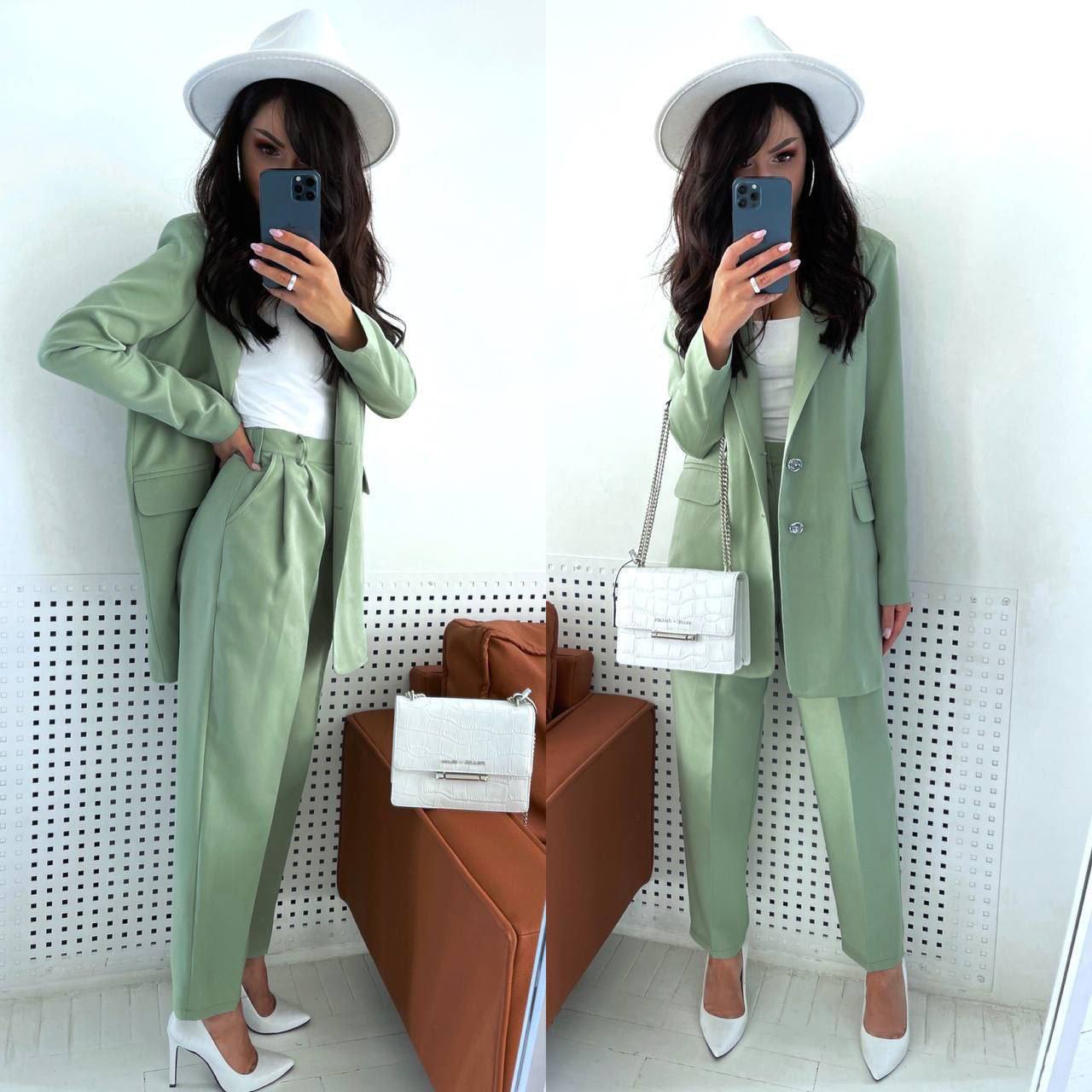 Woman in a green suit with white shoes and hat, standing in front of a mirror.