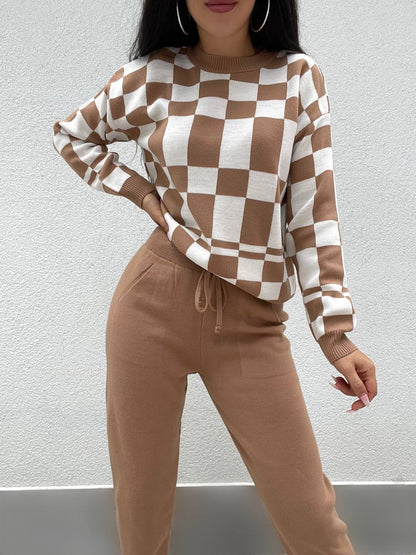Person wearing a brown and white checkered sweater with beige pants against a plain background
