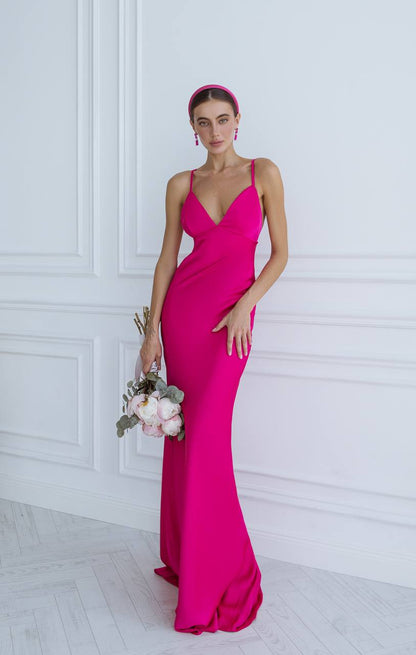 Woman in a bright pink evening gown holding flowers against a white wall.