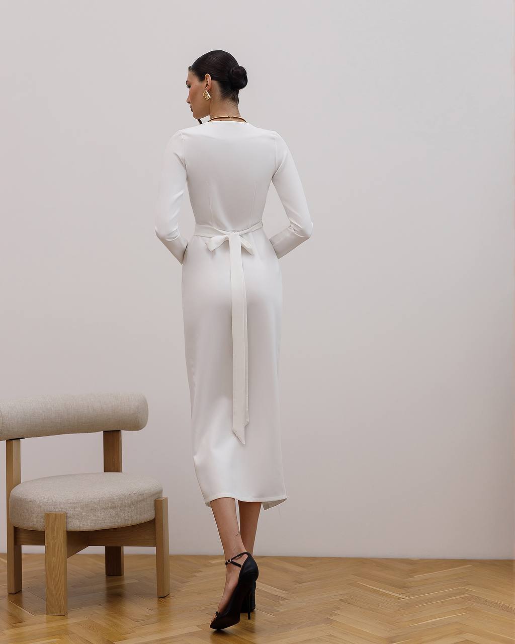 Woman wearing a white dress with a belt in a minimalistic room.