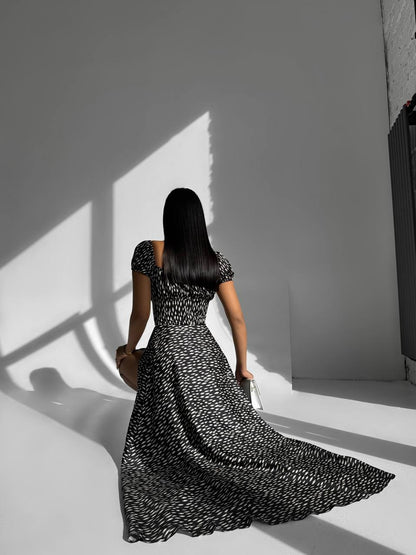 Woman in a black and white patterned dress standing in a room with light casting shadows on the wall.