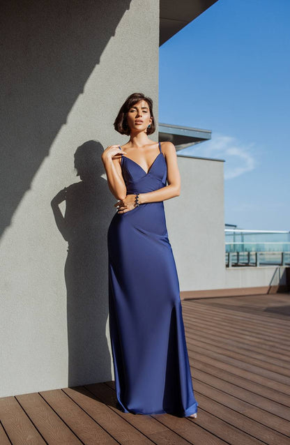 Woman in a blue evening gown standing on a rooftop with a clear sky.