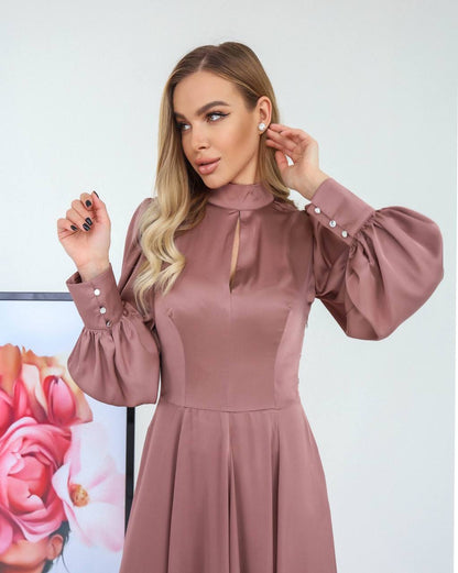 Woman wearing a mauve dress with long sleeves and button details, standing against a white background.