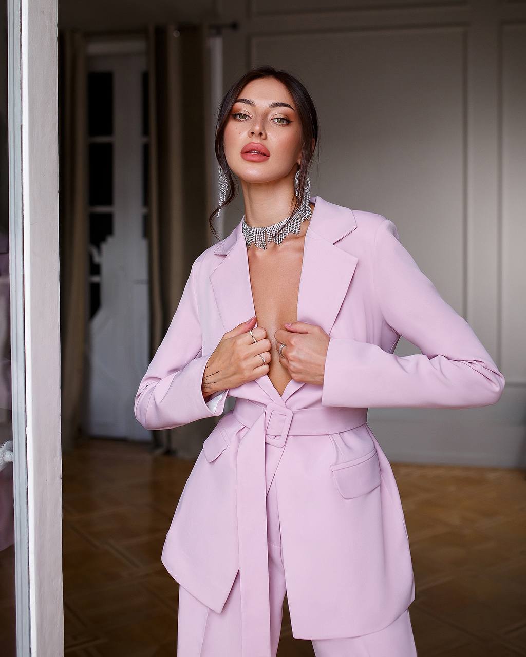 Woman wearing a light pink suit with a choker necklace indoors.