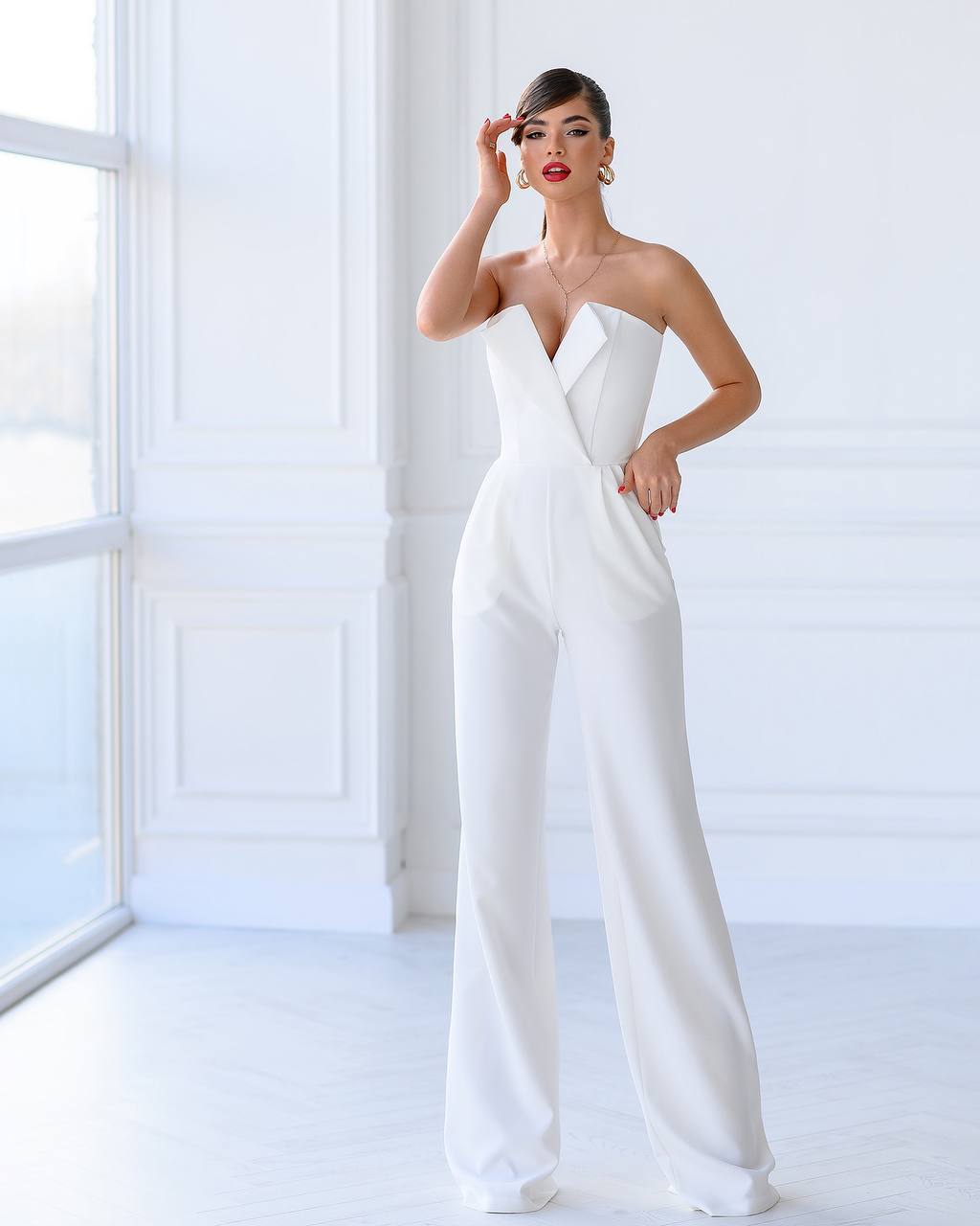 Woman wearing a white strapless jumpsuit in a bright room.
