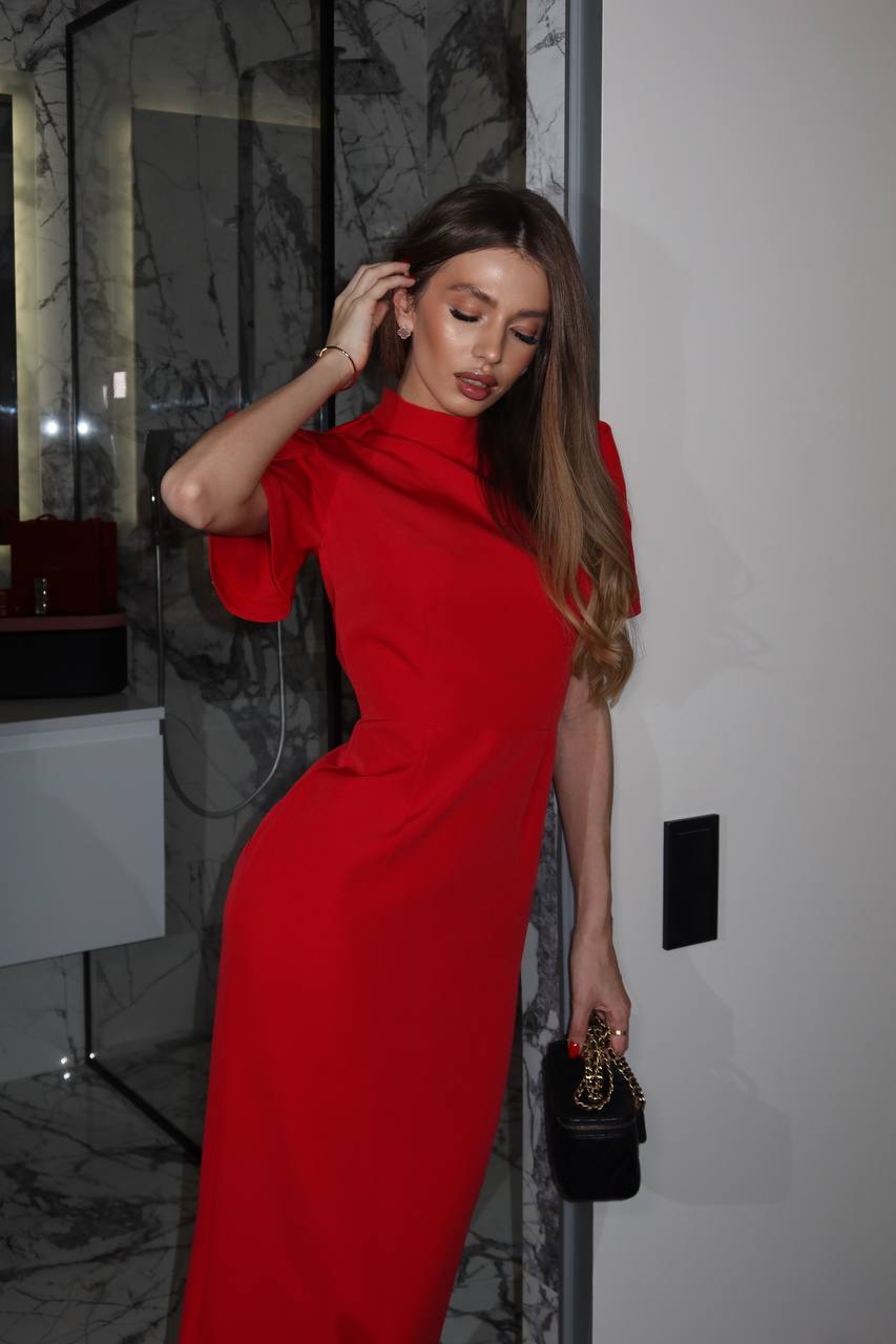 Woman in a red dress standing indoors with a neutral background