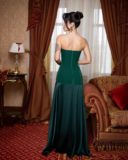 Woman in a green strapless gown standing in an elegant room with red carpet and patterned walls.