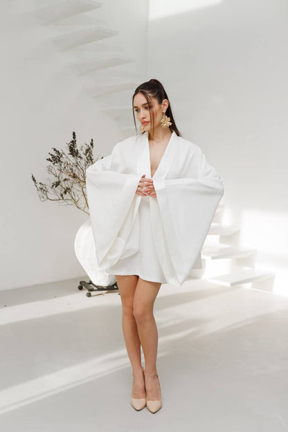 Woman in a white outfit standing in a minimalistic room with a plant.