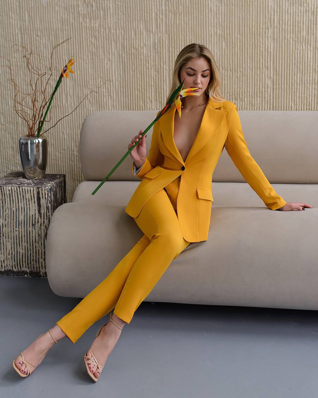 Woman in a yellow suit sitting on a couch holding a flower