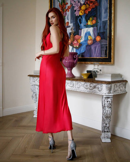 Woman in a red dress standing in a room with decorative table and artwork.