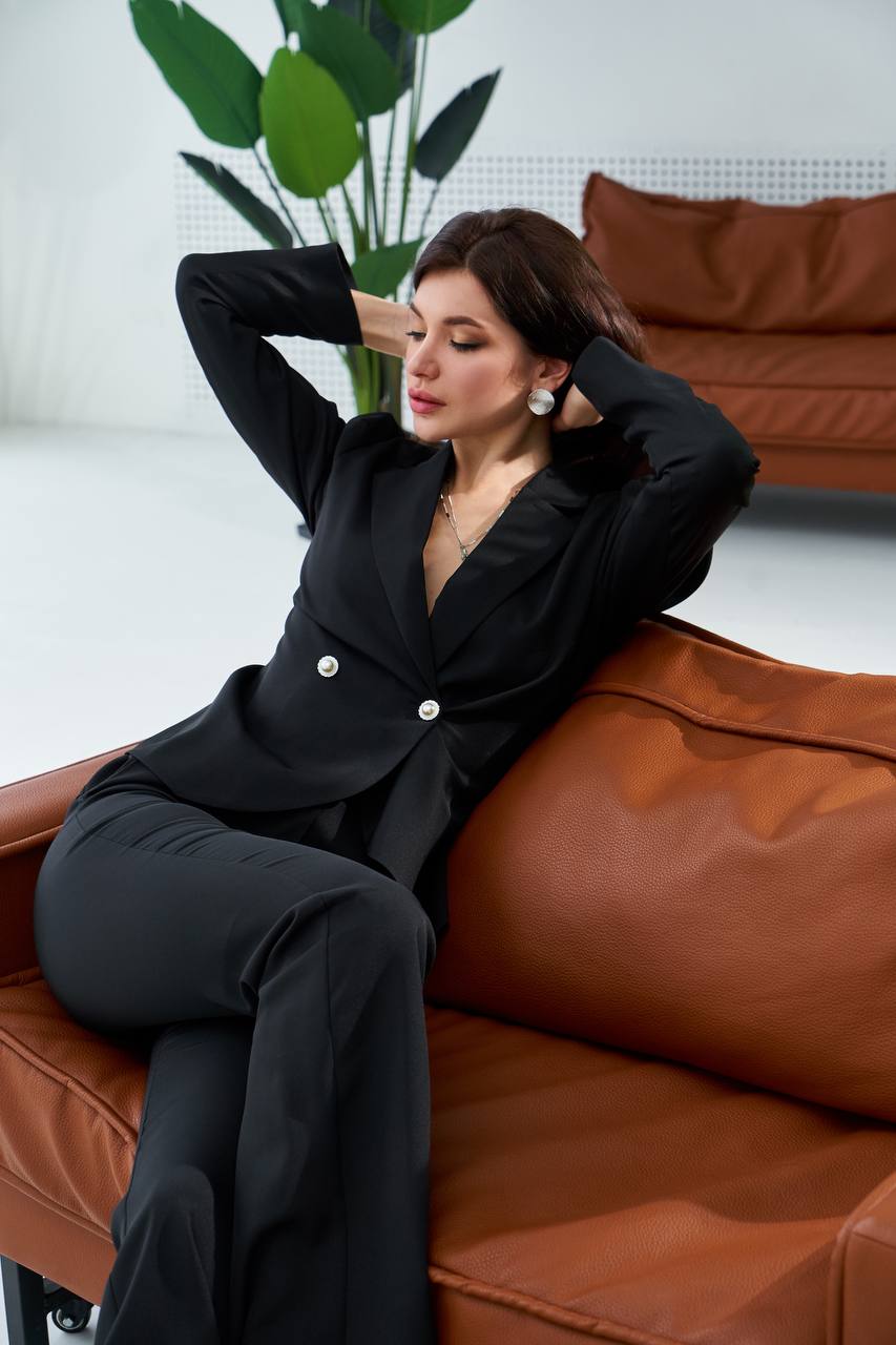 Woman in a black suit sitting on a brown leather couch with a plant in the background