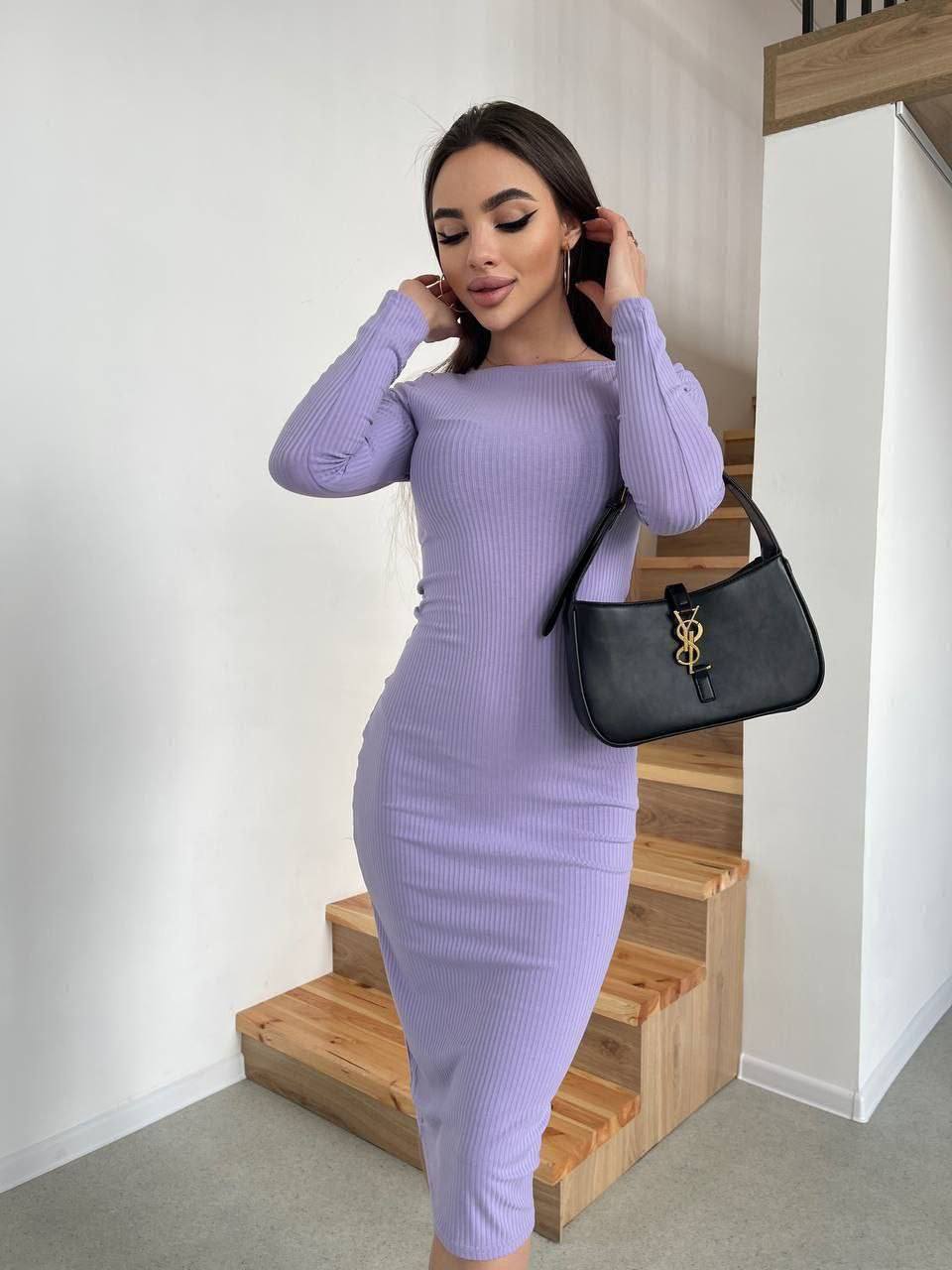 Woman in a purple dress holding a black handbag on wooden stairs.