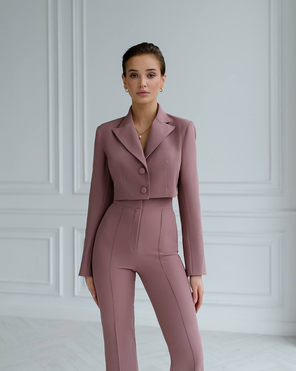 Woman wearing a mauve suit against a white paneled wall