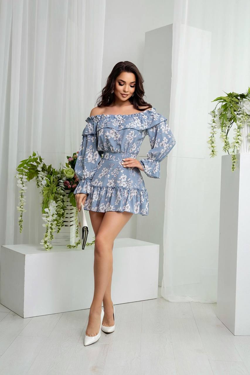 Woman wearing a blue floral dress in a minimalistic setting with plants.