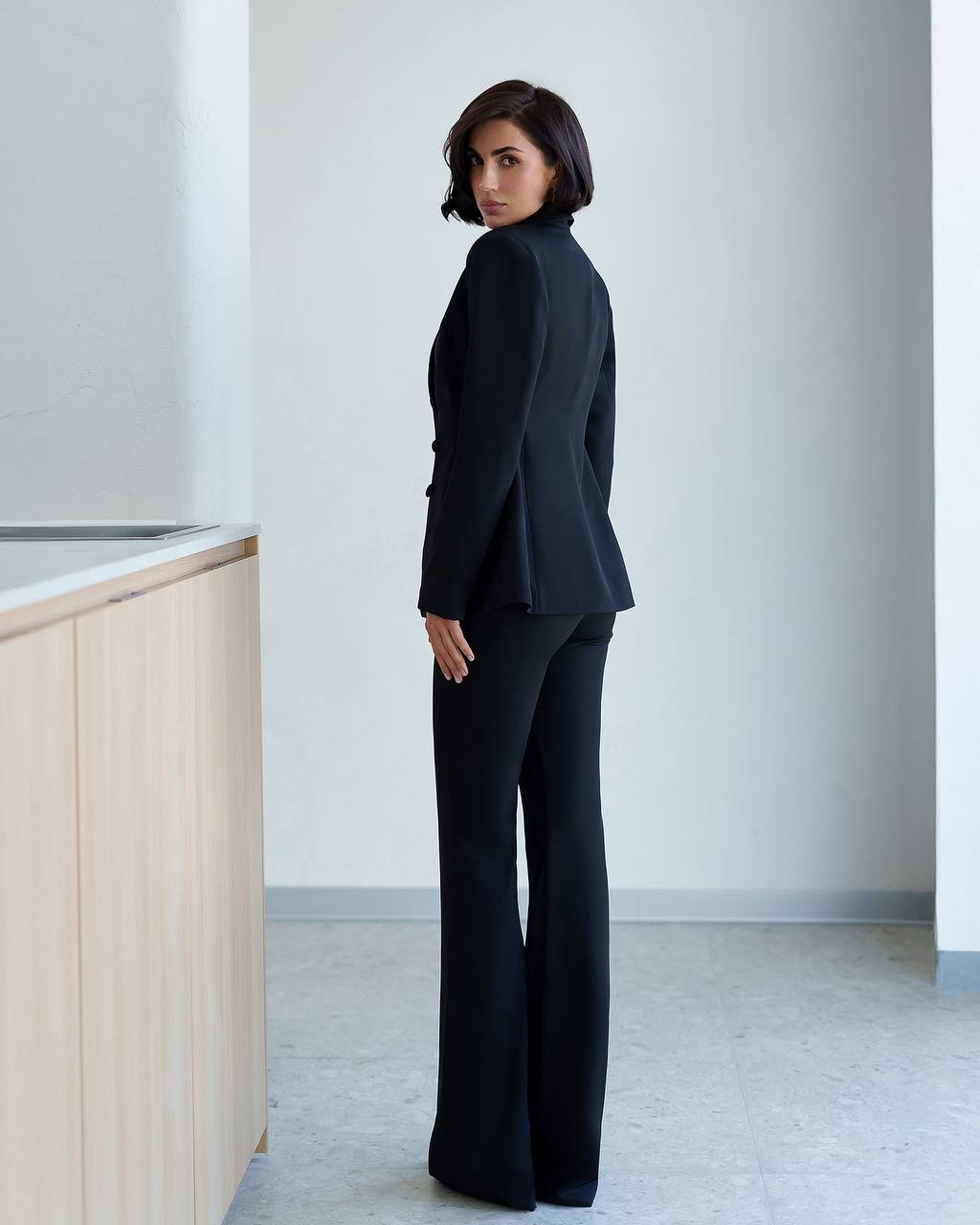Woman wearing a black suit standing in a minimalistic room.