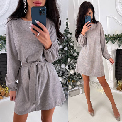 Woman wearing a gray dress in front of a decorated Christmas tree.