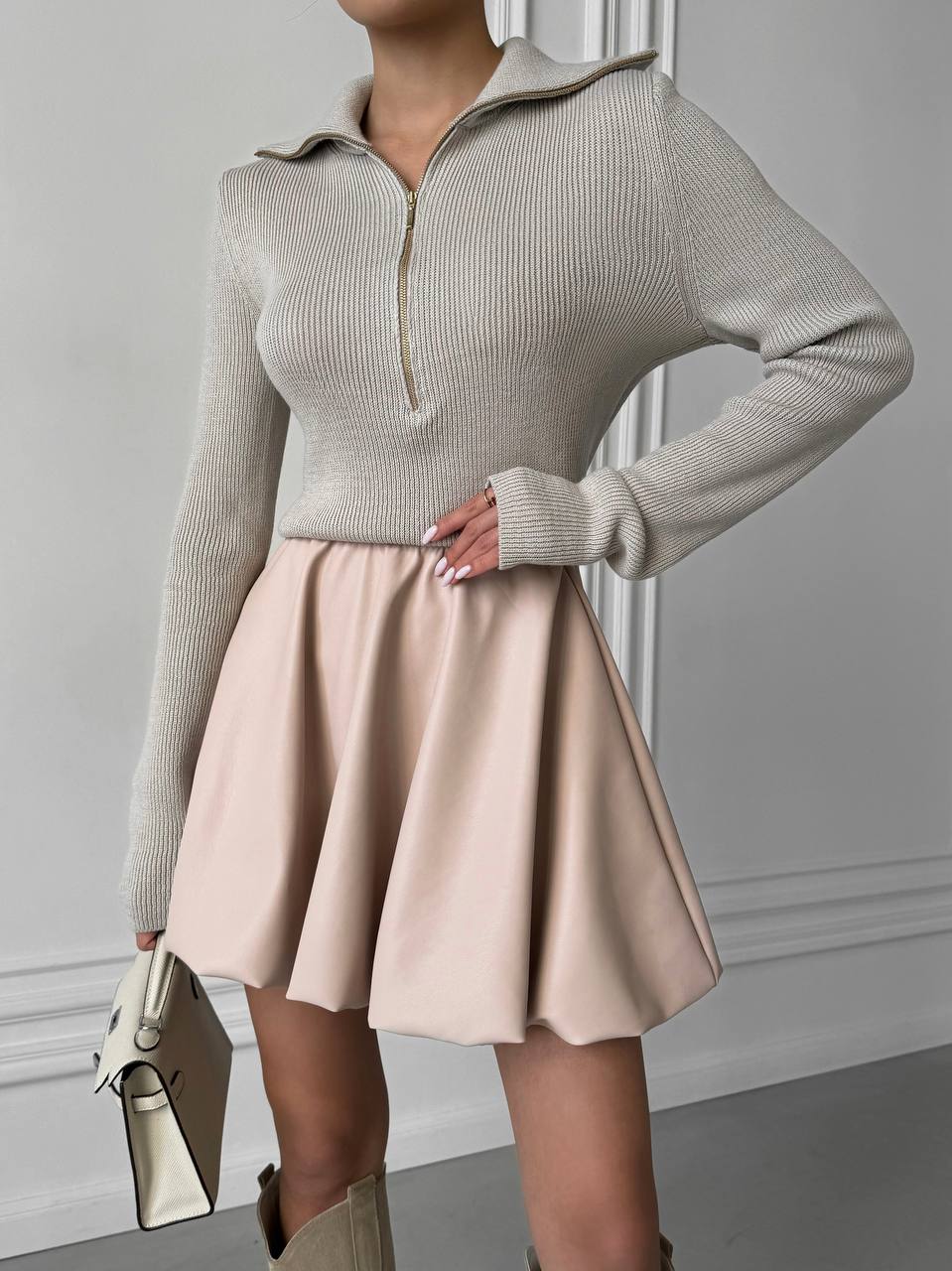 Person wearing a beige sweater and skirt with a neutral background