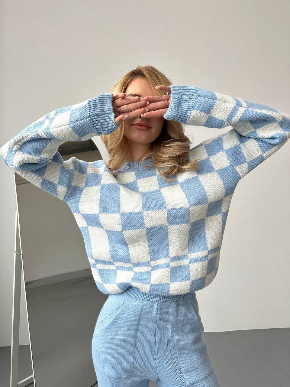 Person wearing a blue and white checkered sweater and pants against a plain background