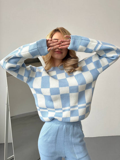 Person wearing a blue and white checkered sweater and pants against a plain background
