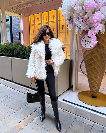 Woman in a white fur coat standing in front of a store window with floral display