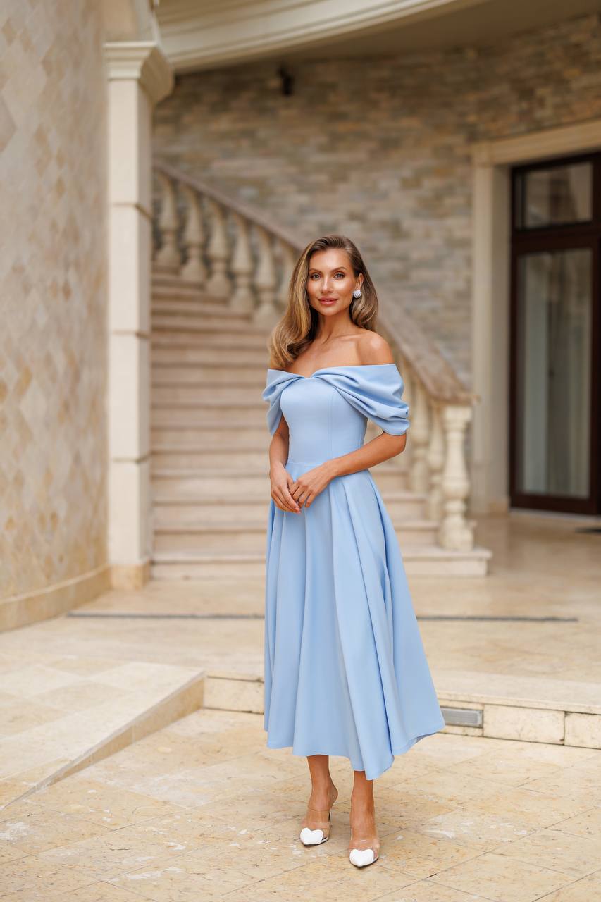 Woman in a light blue off-shoulder dress standing in an elegant outdoor setting.