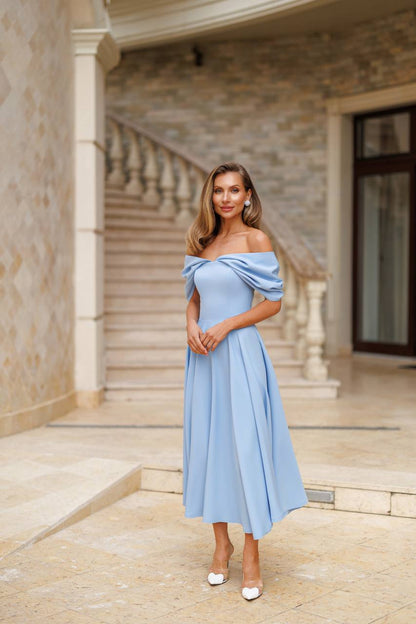 Woman in a light blue off-shoulder dress standing in an elegant outdoor setting.