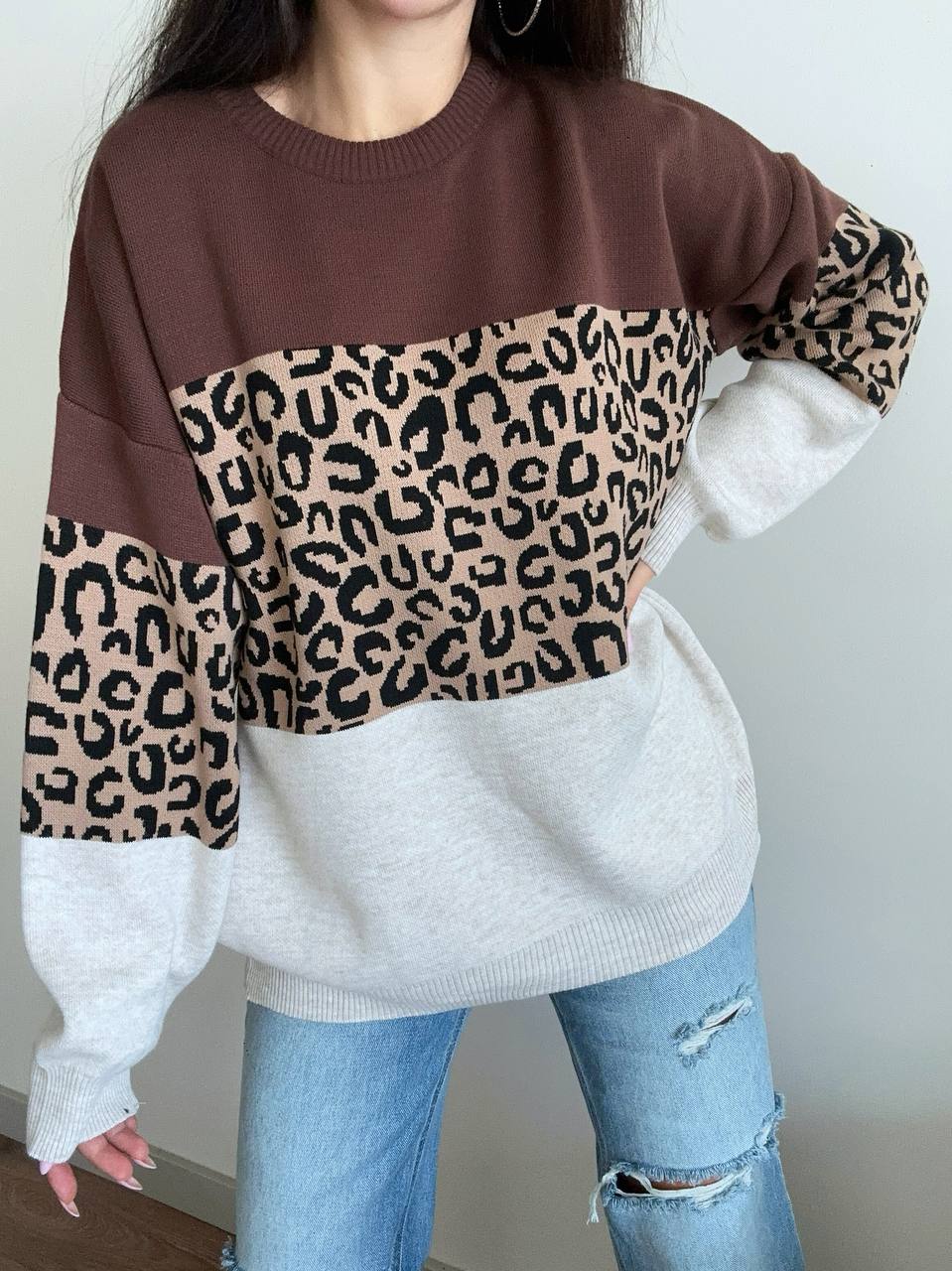 Person wearing a brown, white, and leopard print sweater with light blue jeans.