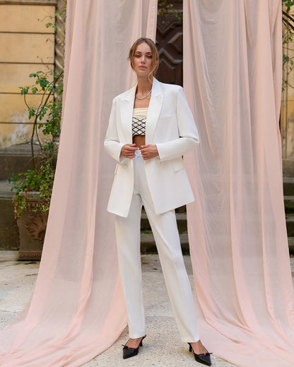 Woman in a white suit standing in front of pink curtains
