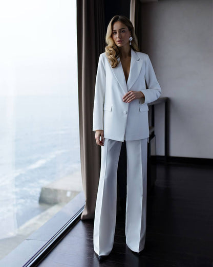 Woman in a white suit standing in a room with large windows.
