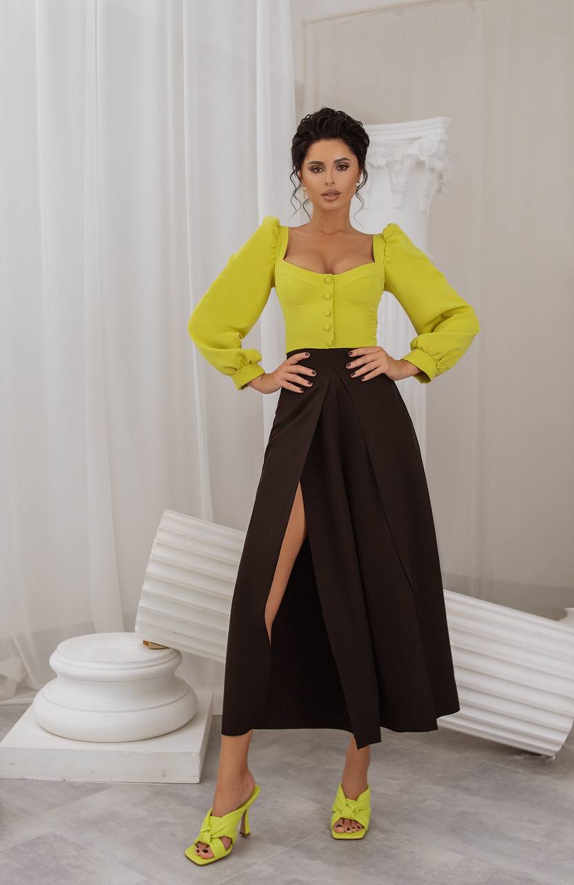 Woman wearing a bright yellow top and black skirt in a minimalistic room.