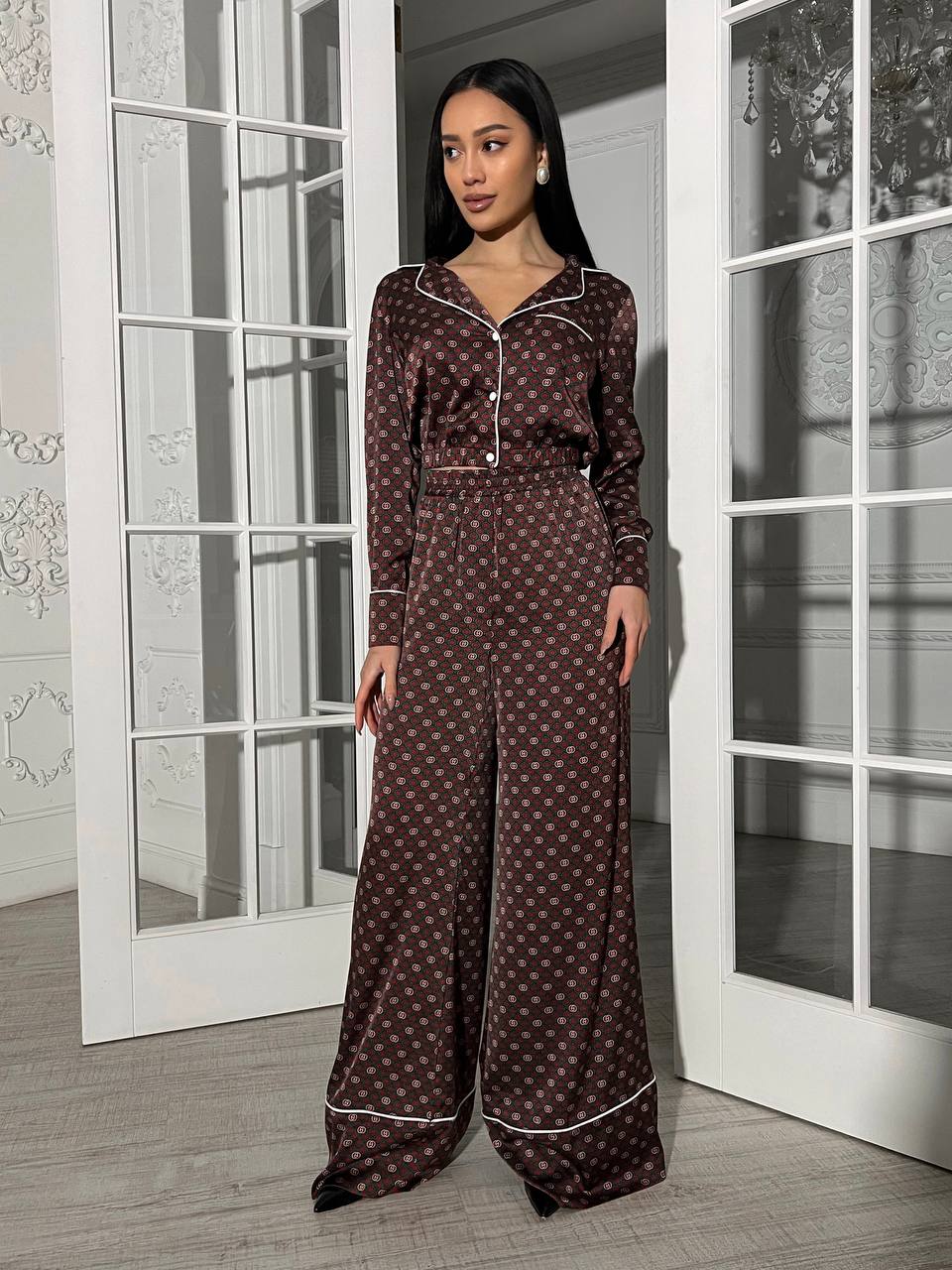 Woman wearing a brown patterned pajama set standing in a room with white doors.