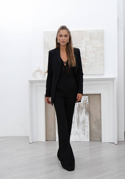 Woman in a black suit standing in a minimalistic room with a fireplace.